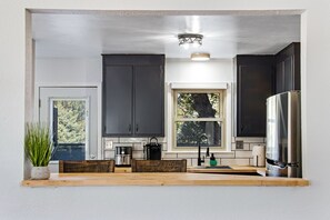A modern kitchen with dark cabinets, a stainless steel refrigerator, a coffee maker, and a window with a view of trees. - Bright Beautiful 2BR Near Broadmoor with King Bed, Hot Tub, Deck & Putting Green (Colorado Springs)