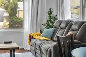 Una sala de estar acogedora con un sofá gris, una mesita y una ventana con cortinas.