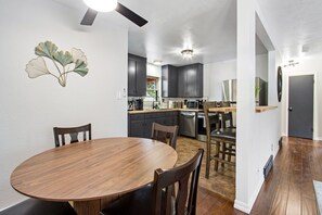 A modern kitchen with dark cabinets, a round wooden dining table, and a ceiling fan. - Bright Beautiful 2BR Near Broadmoor with King Bed, Hot Tub, Deck & Putting Green (Colorado Springs)