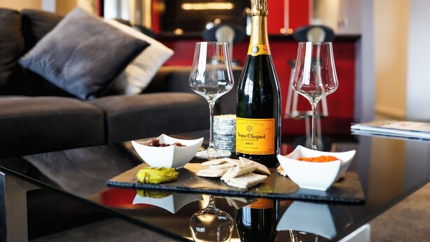 A glass table with a bottle of Veuve Clicquot champagne, two glasses, and small bowls of snacks. - Martinborough Retreat with Hot Tub (Martinborough)