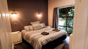 A bedroom with a large bed, two bedside lamps, a window with curtains, and a nightstand. - Martinborough Retreat with Hot Tub (Martinborough)