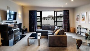 A living room with a sofa, coffee table, TV, fireplace, and large windows. - Martinborough Retreat with Hot Tub (Martinborough)