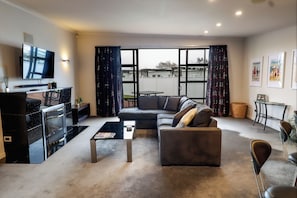Ein Wohnzimmer mit Sofa, Couchtisch, Fernseher, Kamin und großen Fenstern.