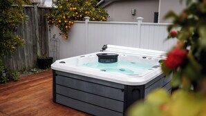 A hot tub in a backyard with a wooden deck, a white fence, and a tree with orange fruit. - Martinborough Retreat with Hot Tub (Martinborough)