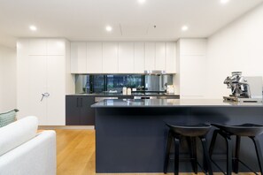 A modern kitchen with a central island, bar stools, and a coffee machine. - Scandi Apartment Above Kingston Dining + Balconies (Kingston)