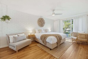 Une chambre à coucher comprenant un lit, un canapé, une chaise, une plante suspendue, une horloge murale et une fenêtre avec des rideaux.