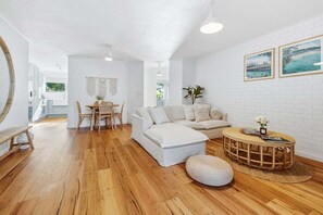 Un salon moderne avec un canapé blanc, une table basse ronde en bois et un coin repas comprenant une table et des chaises en bois.