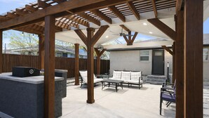 A covered patio area with a grill, outdoor furniture, and a pergola structure. - The Garland Getaway • Backyard Oasis • Family Friendly • Near Dallas (Garland)