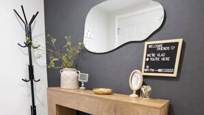 A wooden console table with a mirror, a welcome sign, and a small plant. - The Garland Getaway • Backyard Oasis • Family Friendly • Near Dallas (Garland)