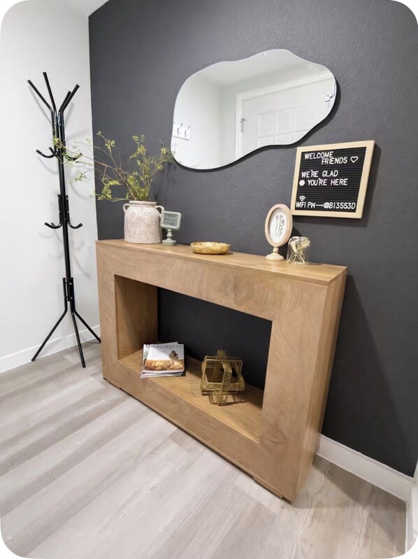 A wooden console table with a mirror, a welcome sign, and a small plant.