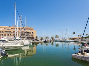 A marina with multiple boats docked, a building with arches, and palm trees. - Port de la Gavine I by Interhome (Hyères)