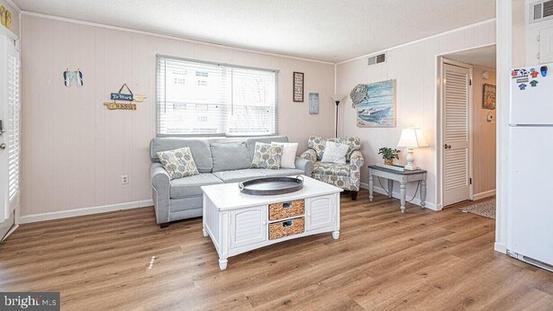 A living room with a sofa, a coffee table, a patterned armchair, a small table with a lamp, and a refrigerator. - Sinbad – Newly Renovated • Steps to the Beach • Midtown OC 2BR 1.5 BA (Ocean City)