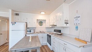 A kitchen with white cabinets, a refrigerator, microwave, stove, and a wooden table. - Sinbad – Newly Renovated • Steps to the Beach • Midtown OC 2BR 1.5 BA (Ocean City)