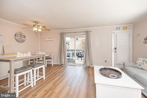 Ein Wohnzimmer mit Deckenventilator, einem Esstisch mit Hockern, einer Couch und einer kleinen Küchenzeile mit Spüle.