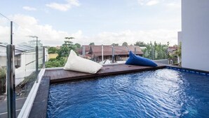 A rooftop pool with a glass balustrade, two pillows, and a view of buildings in the background. - Eclipse Kerobokan (Seminyak)
