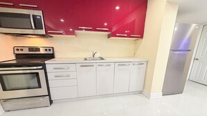 A modern kitchen with stainless steel appliances, white cabinetry, and a red accent wall.
