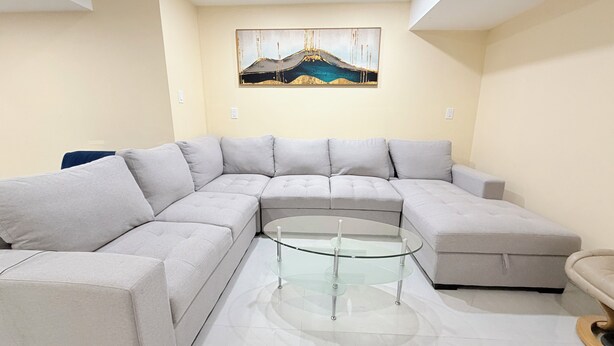 A modern living room with a sectional sofa, a glass coffee table, and a painting on the wall.