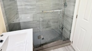 A bathroom with a glass-enclosed shower, a white sink, and a marble-patterned floor.