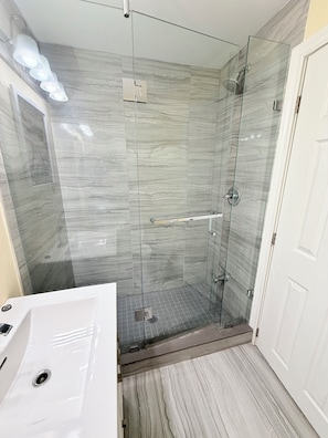 Ein Badezimmer mit einer gläsernen Duschkabine, einem weißen Waschbecken und einem Boden mit Marmoroptik.