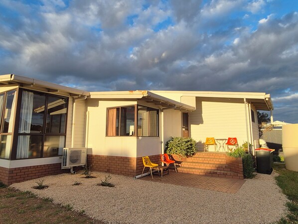 A single-story house with a garage, a small patio with two chairs, and a gravel driveway. - Hopetoun Beach House. Step back in time! A close stroll to town and beach. (Hopetoun)