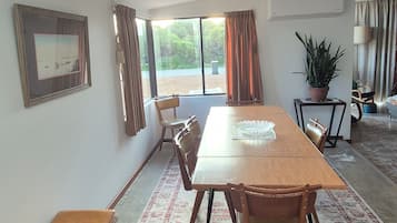 Une pièce spacieuse avec une grande table à manger en bois, plusieurs chaises, un banc, une plante en pot et un tableau encadré au mur.