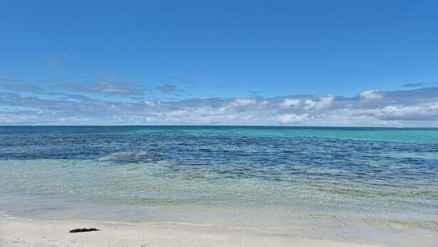 Une plage avec une eau turquoise et limpide, un rivage sablonneux et un ciel partiellement nuageux.