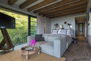 A modern bedroom with a sofa, a TV, and a view of greenery. - Villa Orca (Koh Samui)