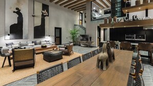 Un vaste espace de vie comprenant une grande table à manger en bois, des sièges confortables, un téléviseur et un escalier menant à un niveau supérieur.