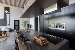 A modern kitchen with a long island, black cabinetry, and a view of the outdoors. - Villa Orca (Koh Samui)