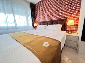 Quarto de hotel com parede de tijolos, cama com roupa de cama branca, manta marrom e decoração floral.