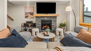 A living room with a fireplace, a flat-screen TV, a sofa, and a coffee table. - Alpine Forest Retreat Sauna + Hot Tub + EV (Canmore)