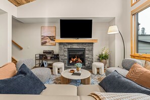 A living room with a fireplace, a flat-screen TV, a sofa, and a coffee table. - Alpine Forest Retreat Sauna + Hot Tub + EV (Canmore)