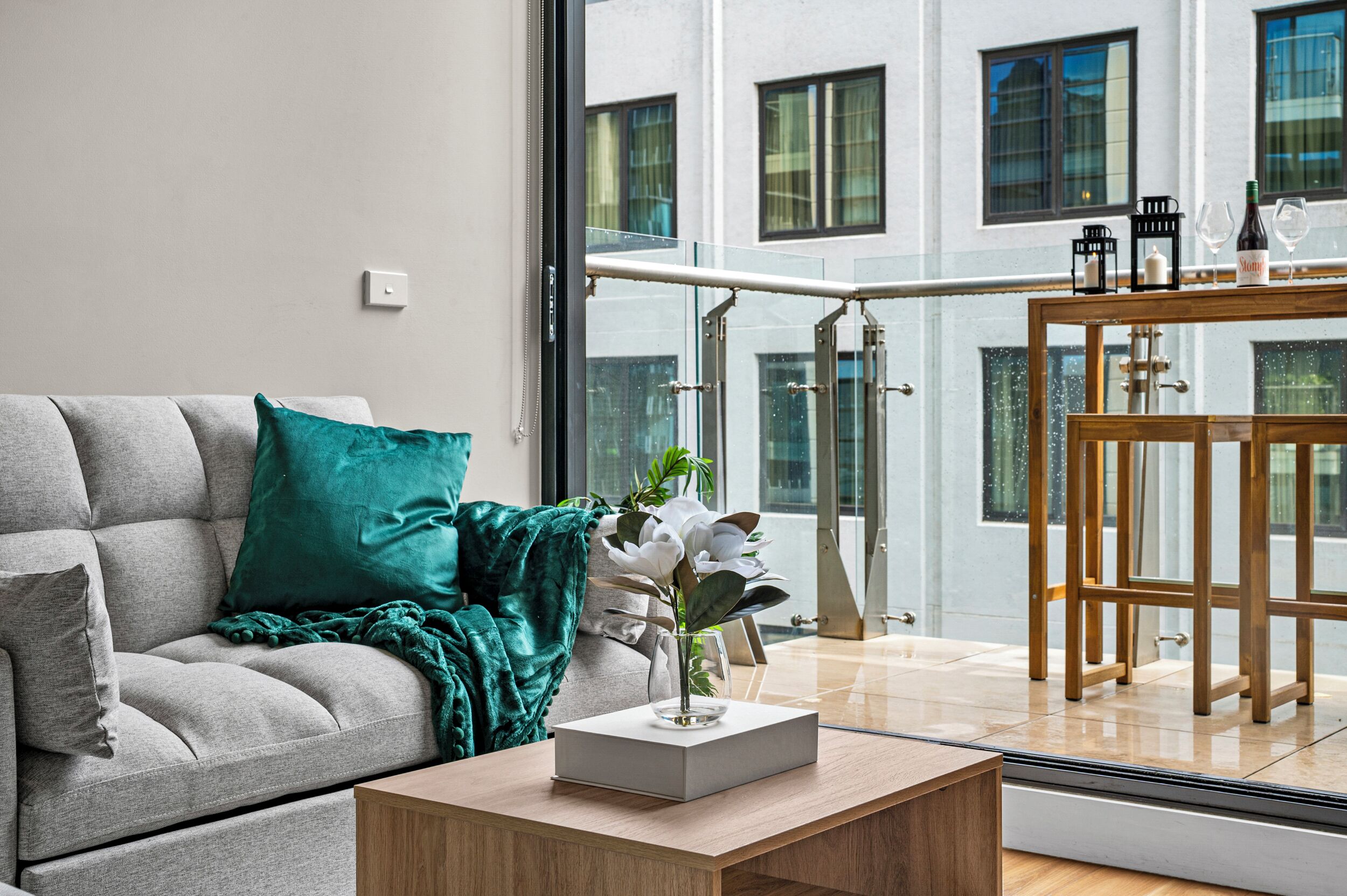 Ein modernes Wohnzimmer mit einem grauen Sofa, einer türkisfarbenen Decke, einer weißen Vase mit Blumen und einem Holztisch.