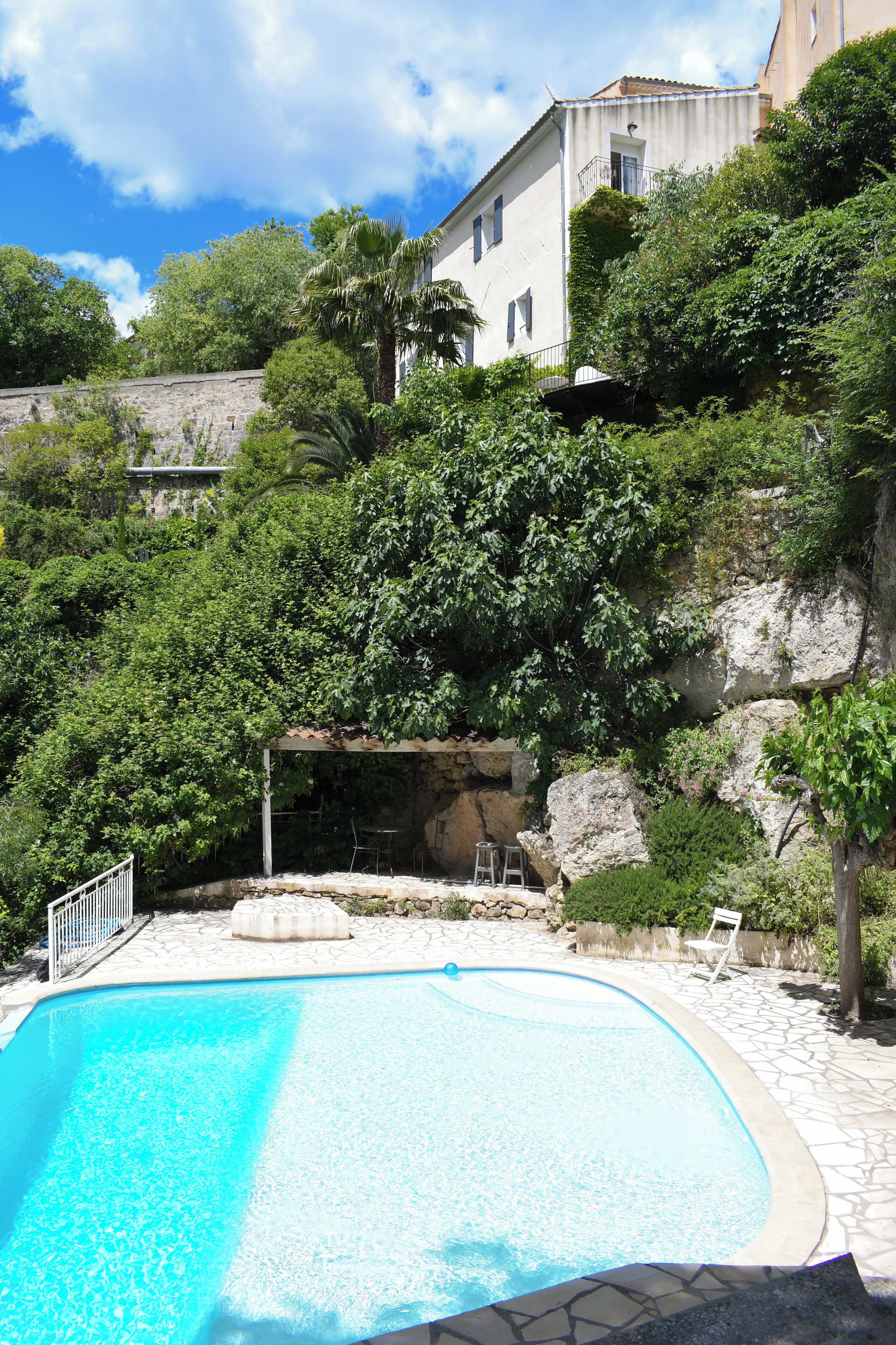 A swimming pool with a stone deck, surrounded by lush greenery and a stone wall.
