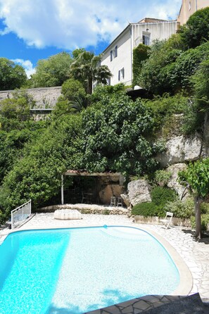 A swimming pool with a stone deck, surrounded by lush greenery and a stone wall. - Le Vieux Moulin Cotignac – Perfect Base to Explore Provence. (Cotignac)