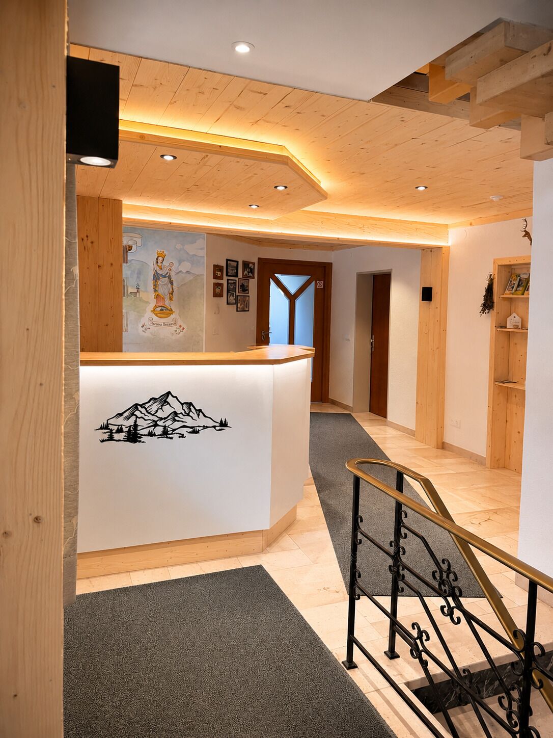 Een receptie met een houten receptiebalie, een trap met metalen leuning, en een wand met ingelijste afbeeldingen en een bergillustratie.