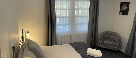 A hotel room with a bed, bedside lamp, window with curtains, chair, and a ceiling fan.