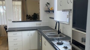 A modern kitchen with white cabinets, a black countertop, a sink, a stove, and a window with blinds.