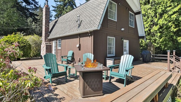 Eine Holzterrasse mit Adirondack-Stühlen, einer Feuerstelle und einem überdachten Grillbereich.