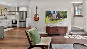 Eine moderne Küche mit Edelstahlgeräten, ein Essbereich mit Holztisch, eine gemütliche Sitzecke mit grüner Kissenlehne und ein großer Flachbildfernseher an der Wand.