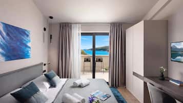 Habitación de hotel con cama, escritorio, silla, vista al mar y un cuadro en la pared.