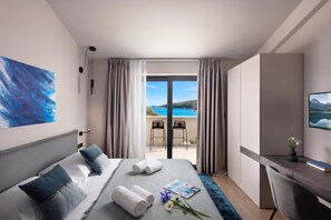 Quarto de hotel com cama, escrivaninha, cadeira, vista para o mar e um quadro na parede.