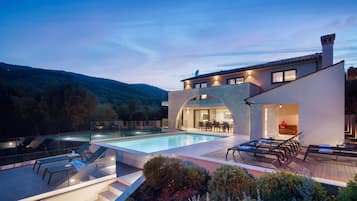 Una villa moderna con piscina, mobiliario exterior y vistas del paisaje circundante.
