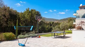Una cancha de baloncesto al aire libre con aro, una mesa de ping pong y una mesa de tenis.
