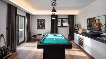 A modern room with a pool table, a guitar, and a dining area with a TV.