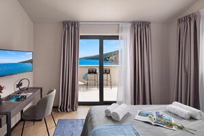 Ein Hotelzimmer mit einem Bett, einem Schreibtisch mit Stuhl, einem Fernseher und einem Balkon mit Meerblick.