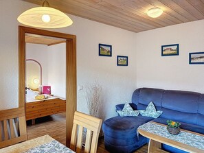 Une pièce avec un plafond en bois, un canapé bleu, une chaise en bois, une petite table avec une plante et des tableaux encadrés accrochés au mur.