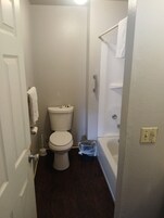 Un baño pequeño y estrecho con un inodoro, una ducha y un cubo de basura.