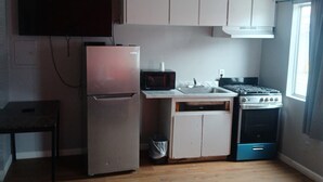 Cocina compacta equipada con refrigerador, microondas, estufa y ventilador de techo.