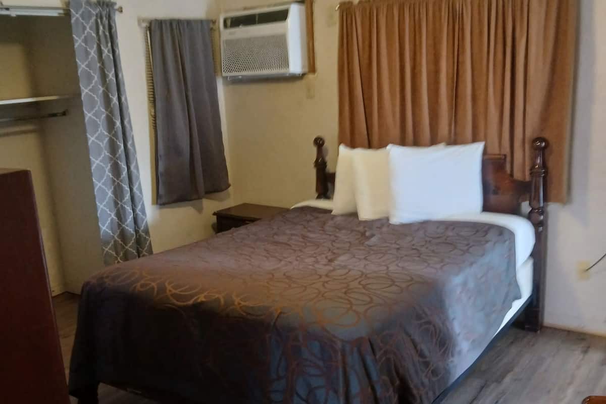 A bedroom with a bed, a ceiling fan, an air conditioning unit, and a wooden floor.